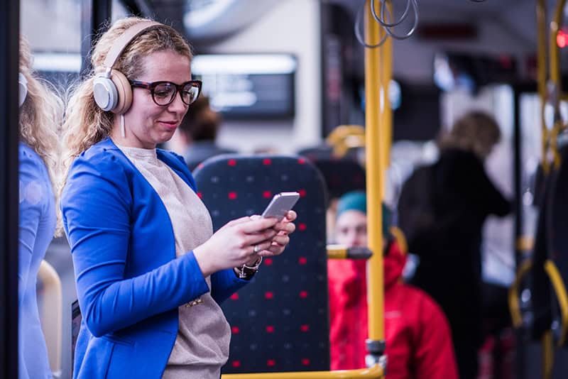  En kvinne med hodetelefoner bruker en smarttelefon til å delta i digital læring mens hun er på bussen.