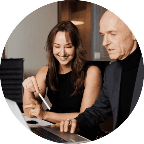 Two people collaborating at a laptop, smiling and engaged in discussion in an office setting.