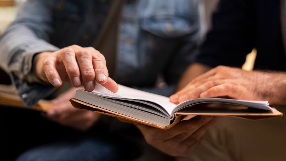 To menn blar i en bok mens de diskuterer innholdet